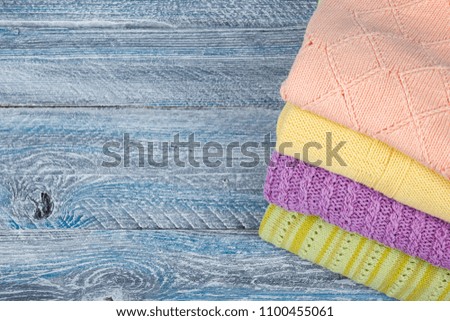 Knitted wool sweaters. Pile of knitted summer, autumn clothes on blue, wooden background, sweaters, knitwear, space for text.