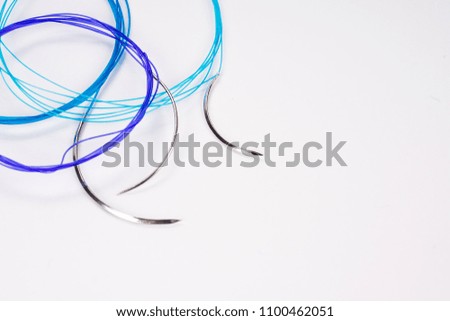 Colorful surgical nylon monofilament suture with curved needle isolated on an abstract blurred white background. Healthcare, medical and surgery concept. Detailed close up with soft selective focus