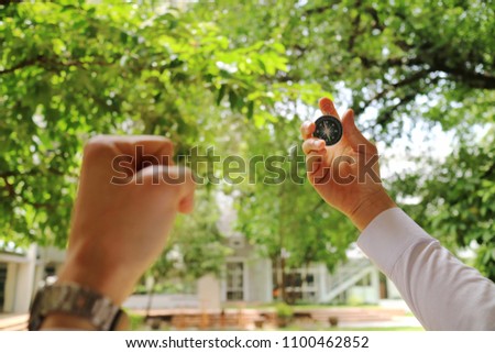 A hand holding a compass and a hand hold a fist, just meaning the new way to successful business. Keep walking. Selective focus with blurred green leaves and building background.