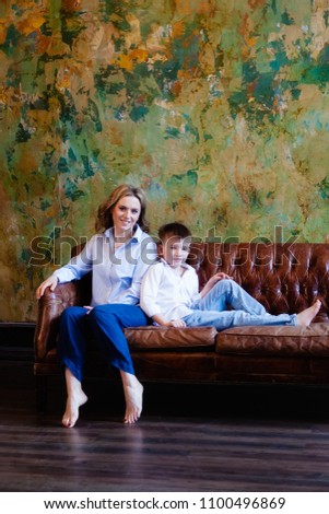 A woman and her son are sitting on the couch in the room, they are looking at the camera and smiling
