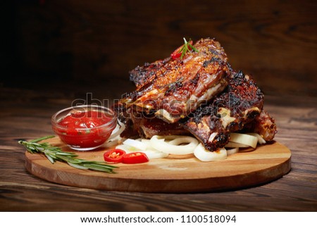 Fried ribs with rosemary, onion, sauce on a wooden round Board. Dark background. Place for text, copyspace Royalty-Free Stock Photo #1100518094