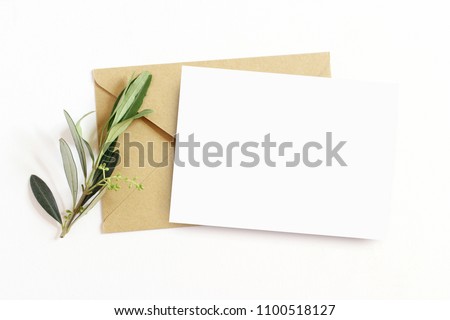 Feminine stationery,  desktop mock-up scene. Blank greeting card and craft envelope with olive branch.White table background. Flat lay, top view. 