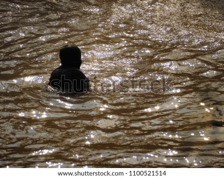 People are swimming in the river during sunset. It looks like gold water and glistening at the surface.