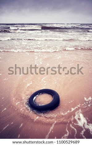 Old black rubber tire left on a beach, environment pollution concept, selective focus, color toned picture.                            