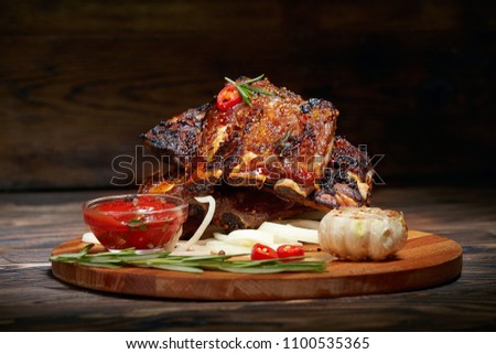 Fried ribs with rosemary, onion, sauce on a wooden round Board. Dark background. Place for text, copyspace Royalty-Free Stock Photo #1100535365