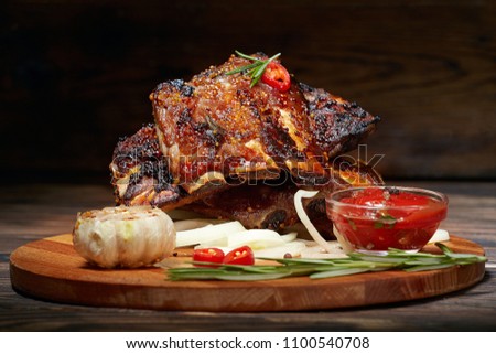 Fried ribs with rosemary, onion, sauce on a wooden round Board. Dark background. Place for text, copyspace Royalty-Free Stock Photo #1100540708