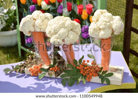 The composition of cauliflower and carrots in plastic transparent cups for fruit juice is on the table in the summer garden 