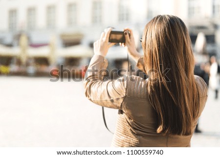 Tourist taking photo of town square during vacation with camera. Woman taking holiday picture in city. Tourism concept. Back view of female person.