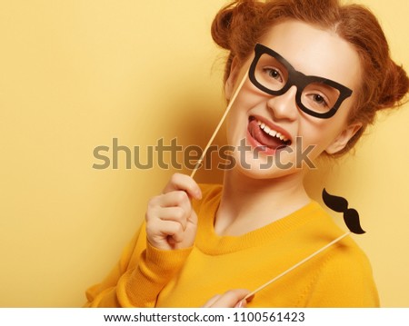 lifestyle and people concept: Happy girl  wearing fake mustaches and glasses over yellow background. 