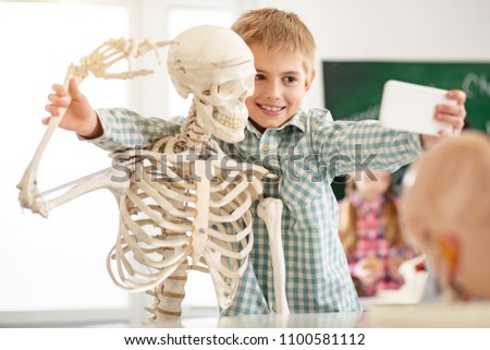 So cool. Cheerful nice boy holding a skeletons hand while taking a photo with it