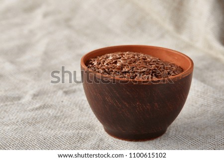 Top view close-up picture of flax seeds in a clay bowl on homespun tablecloth, selective focus.