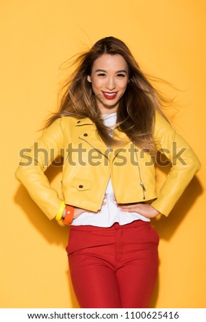 attractive young asian woman in leather jacket posing on yellow background 