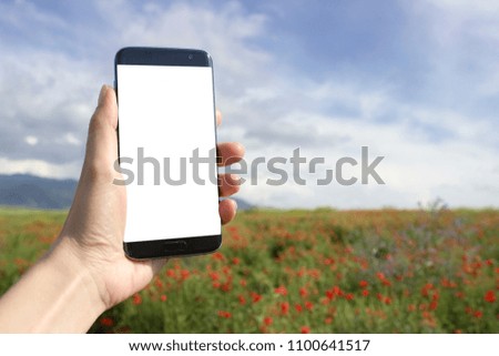 Adult hand holding smart phone mock up over beautiful countryside poppy field landscape background