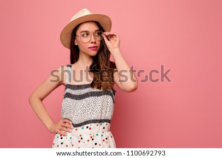 Romantic beautiful young lady dressed summer hat and bright dress, in glasses posing on pink background. Studio shot of inspired white girl with curly long  hair waving.