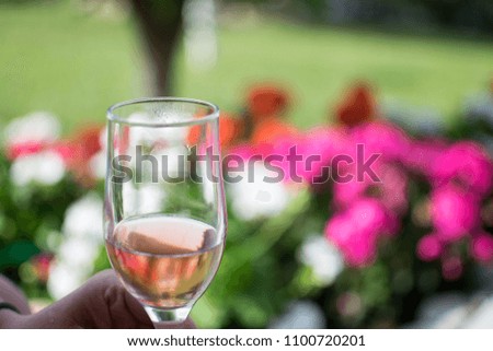 Female hand holding rose wine glass on a colorful flowery background.