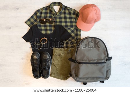 Stylish women's or teenager's clothing set with accessories: checkered shirt, black top, green jeans shorts, pink cap, grey backpack, sunglasses, bracelet and boots in military style. Summer outfit