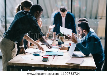 Collaborative process of multicultural skilled students during brainstorming meeting in office.Diverse team of young people dressed in formal wear cooperating on developing common design project Royalty-Free Stock Photo #1100733734