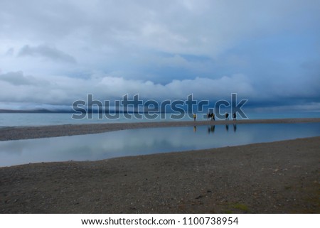 extremely low monsoon clouds over a highland lake (Namtso, Tibet); cold summer morning; group of tourists take a picture; Tibet
