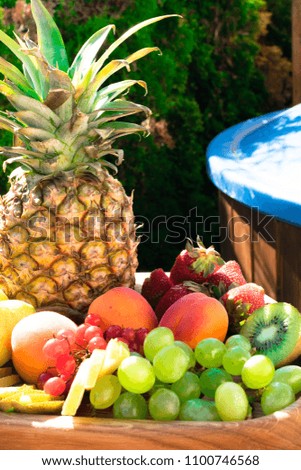 Mix of different exotic fresh colorful fruits on dark wooden table and green trees