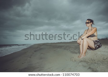 A young woman alone on the beach with a storm brewing on the horizon
