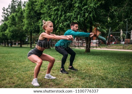 Healthy young man and woman doing squat exercises outdoors.