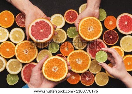 Choose your citrus. Many hands holding various fruits at black background, top view