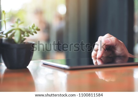 Closeup image of a woman's hands pointing , touching and using tablet pc with tree pot on table