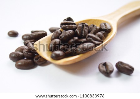 Dark roasted coffee beans on a wooden spoon over a  white background with a selective focus. The roast level allows oils to be seen on the beans 
