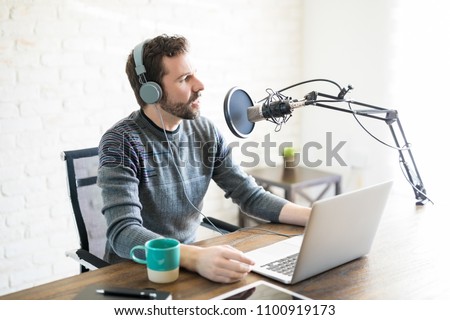 Hispanic young man with headphones and laptop talking on mic, online radio.