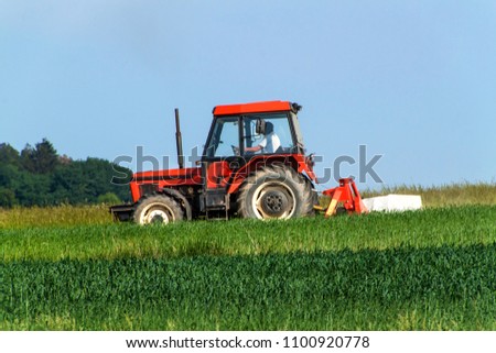 Old red tractor sails the meadow. Summer work on an agricultural farm
