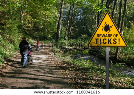 Warning sign "beware of ticks" in infested area in a park with walking family