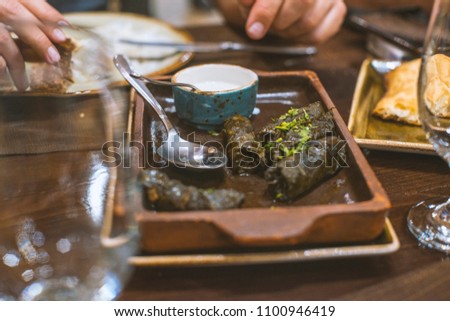 Dolma - stuffed grape leaves with meat and rise, sauce with Greek yogurt in clay plates in Middle Eastern restaurant, leftovers after dinner. Hands holding food in background