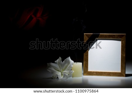 Blank thin brown picture  frame, with smoky candle and white lily flower on dark background with red decoration