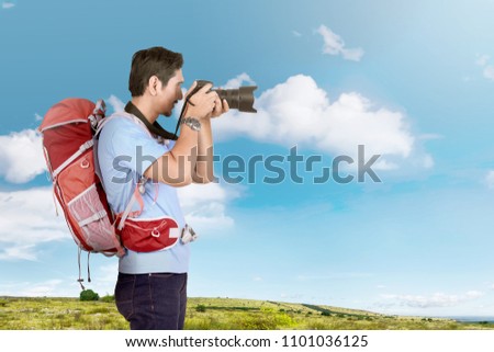 Side view of asian photographer man with backpack on the meadow field