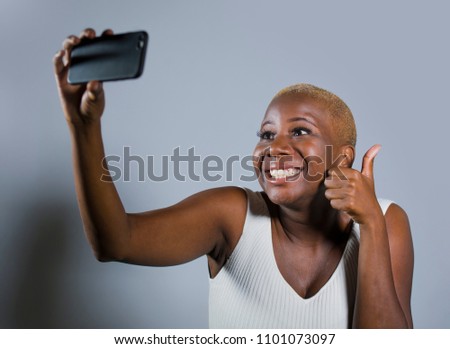 young beautiful and happy black afro American woman smiling excited taking selfie picture portrait with mobile phone recording self portrait video posing cheerful having fun giving thumb up isolated