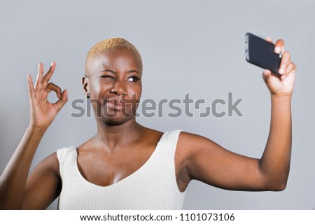 young beautiful and happy black afro American woman smiling excited taking selfie picture portrait with mobile phone or recording self portrait video posing cheerful having fun giving ok fingers