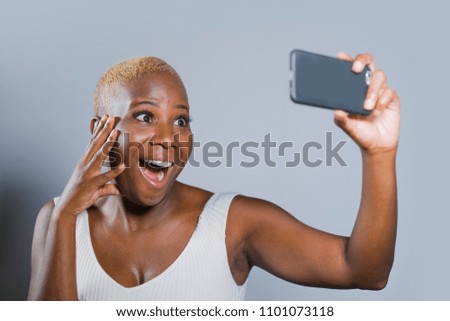 young beautiful and happy black afro American woman smiling excited taking selfie picture portrait with mobile phone or recording self portrait video posing joyful having fun on isolated background