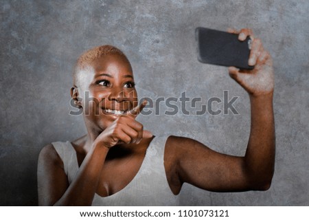 young beautiful and happy black afro American woman smiling excited taking selfie picture portrait with mobile phone or recording self portrait video posing joyful having fun on isolated background