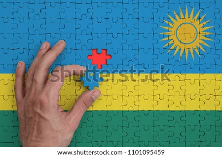 Rwanda flag  is depicted on a puzzle, which the man's hand completes to fold