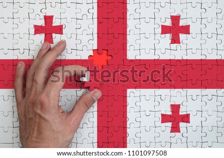 Georgia flag  is depicted on a puzzle, which the man's hand completes to fold