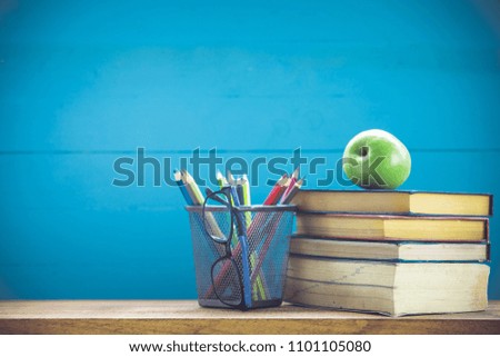 Composition of books, stationery and an green apple on the desk in the background of the blackboard