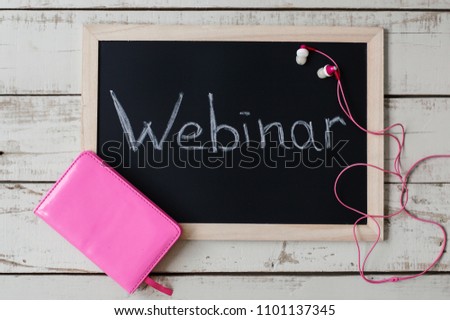Webinar concept. Blackboard with handwritten text "Webinar", pink notebook and earphones on wooden background, top view