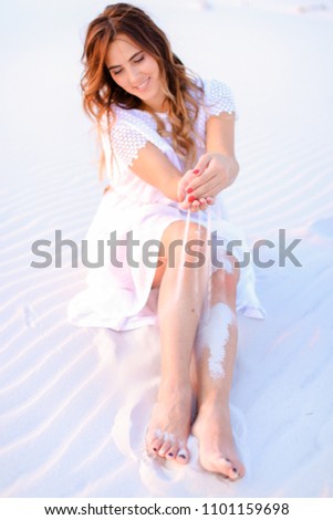 Young caucasian female person sitting on white sand and wearing dress. Concept of beauty and resting on beach, summer seasonal photo session.