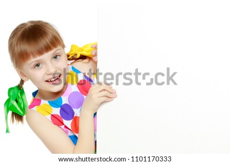 A beautiful Caucasian little blonde girl with long pigtails, in which large colored bows are braided, and a short bangs on her head. In a short summer dress.Looks because of the white obstacle.