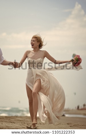 Romantic couple Happy beautiful young laughing bride in beige dress holding wedding bouquet of coral roses running on sea beach coast on blue sky background, vertical picture