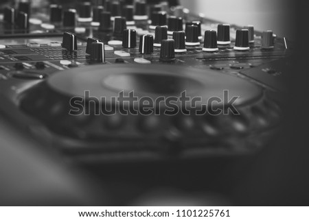 Closeup of dj musical mixer professional console black color with many buttons and knobs in night club or studio.