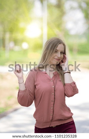 Beautiful girl listening music and dancing in the park covered by sunlight in the background