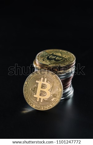close up view of bitcoin leaning on stack of various bitcoins on black background