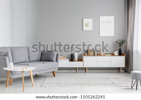 Grey settee near white cupboard in minimal living room interior with posters on the wall. Real photo Royalty-Free Stock Photo #1101262241