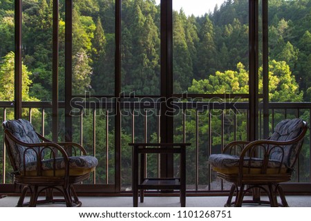 An interior with two comfortable chairs besides large veranda windows on a deck, with a beautiful view of a  sunlit forest outside. Royalty-Free Stock Photo #1101268751